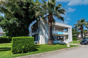A modern two-story building with a sign reading "ACCUEIL" on the ground floor, surrounded by well-maintained greenery and palm trees. - Carre Marine N°105 - 3P6 (Mandelieu-la-Napoule)