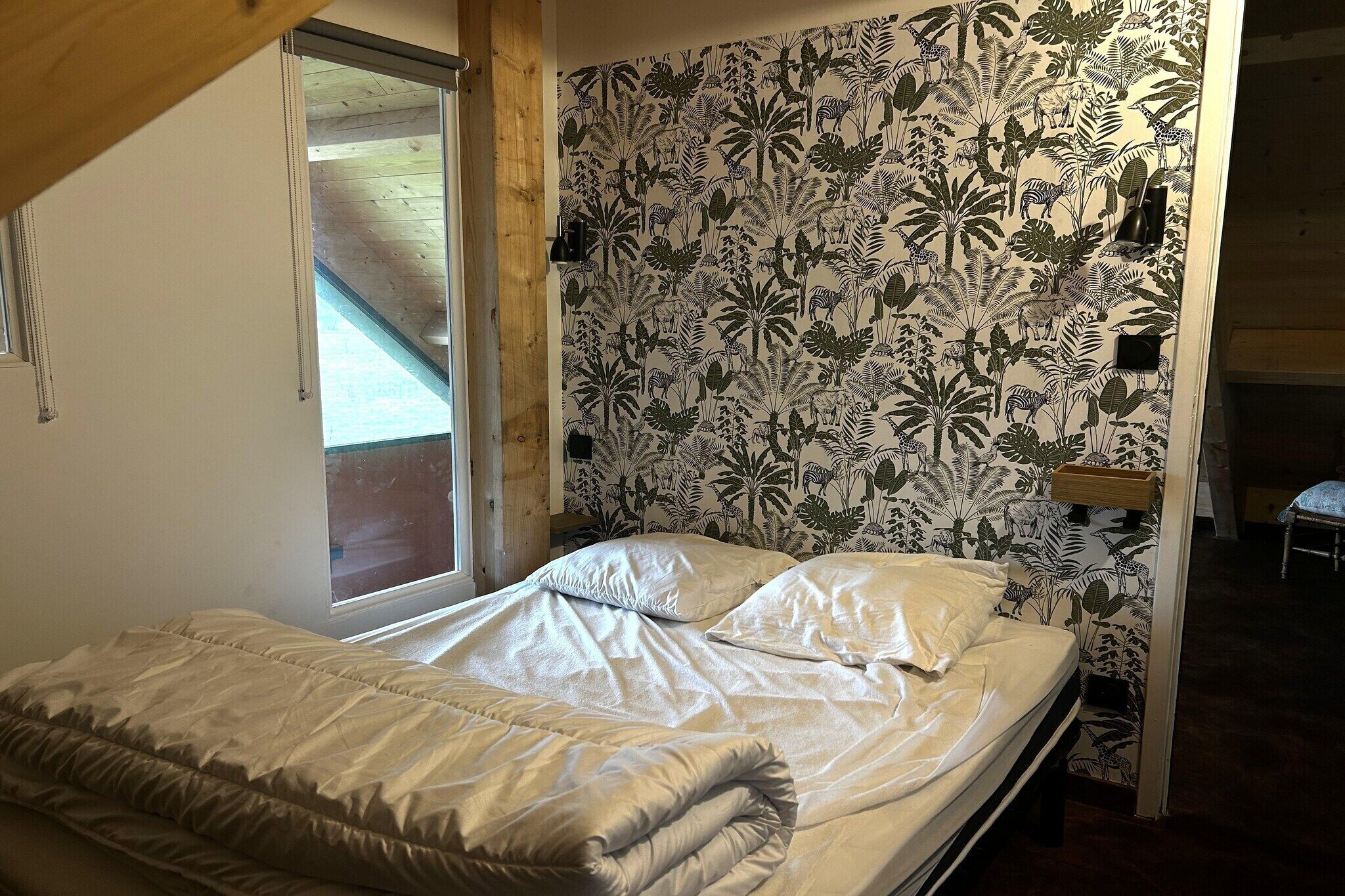 Quarto com cama, janela e parede decorada com papel de parede de planta tropical.