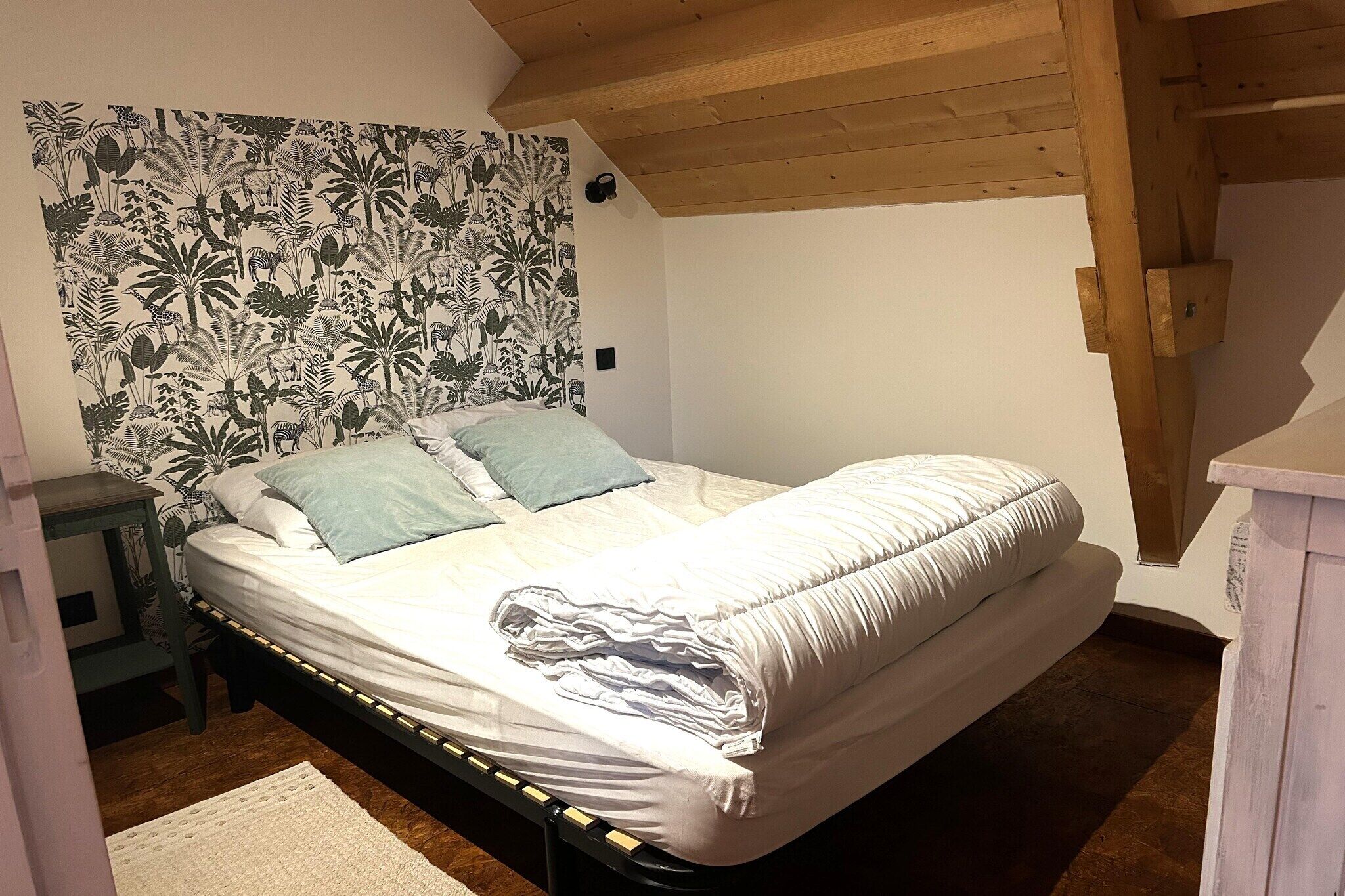 Ein Schlafzimmer mit einem Bett, einem Nachttisch, einer Holzbalkendecke und einer Wand mit floralem Muster.