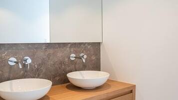 Une salle de bain avec deux vasques blanches posées sur un meuble-lavabo en bois, un grand miroir au-dessus et un pare-baigneoire en marbre.