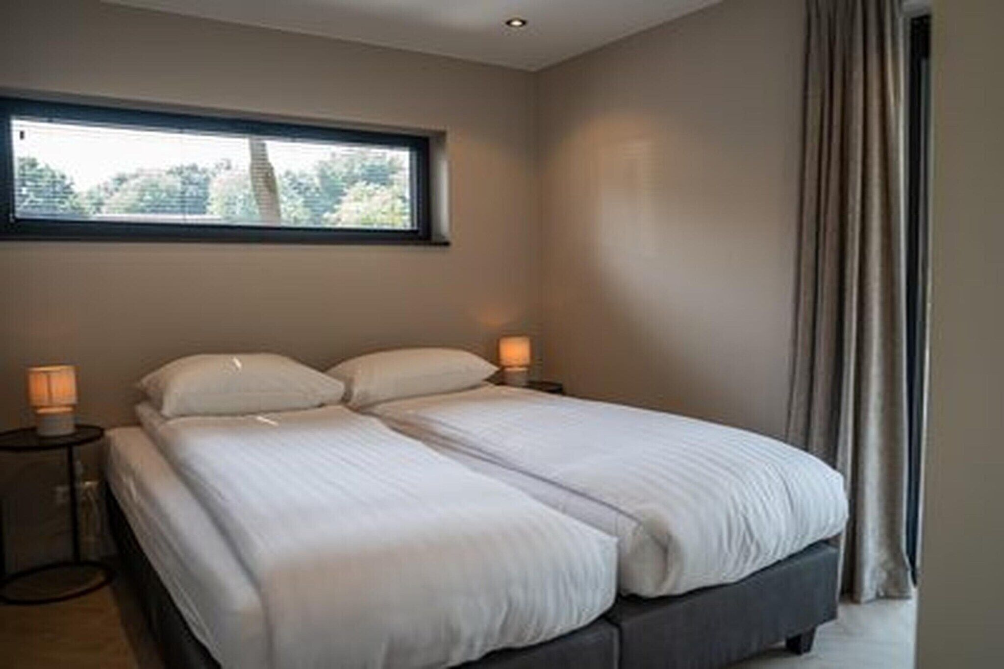 A bedroom with a bed, two bedside lamps, a window, and a curtain.