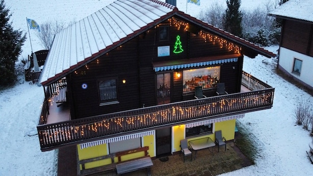 Uma cabana de madeira com varanda, placa de árvore de Natal e luzinhas.