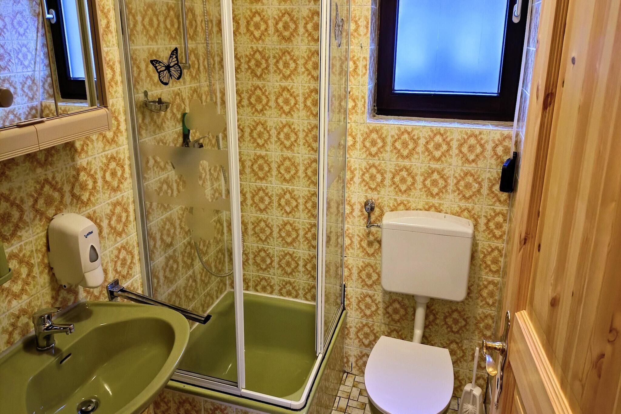 Une salle de bain avec un lavabo vert, une douche en verre, des toilettes et des carreaux à motifs.