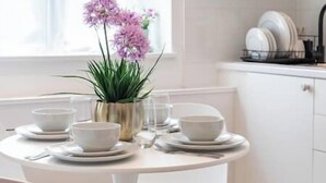 A dining table set with white bowls and plates, a vase with purple flowers, and a window in the background. - New! Delightful 2BR Flat in Woolwich (Greater London)