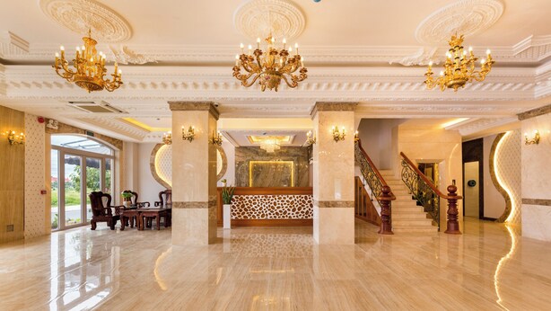Un'ampia hall con pavimento in marmo, lampadari decorati, una reception e una scalinata.