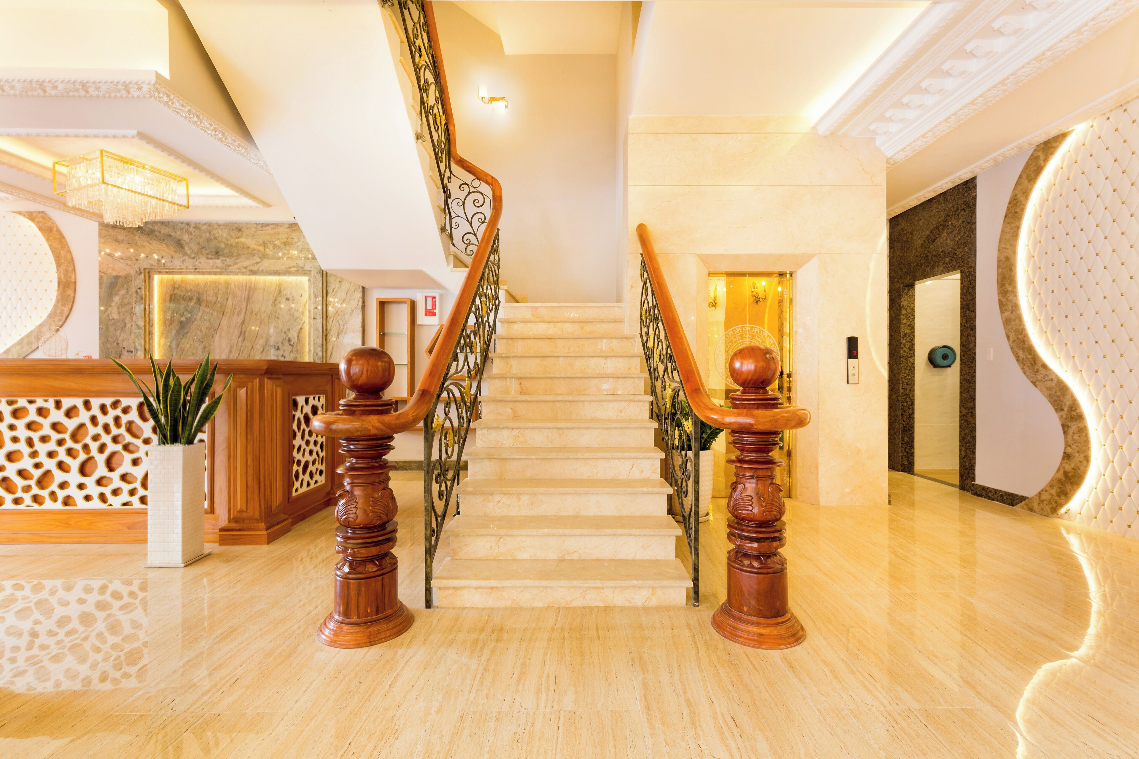Una imponente escalera de mármol con barandillas de madera que conduce a un rellano con una recepción y una planta en maceta.