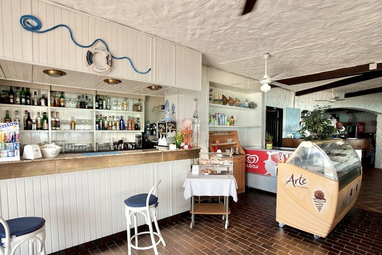 A bar area with a wooden counter, stools, and a dessert display.