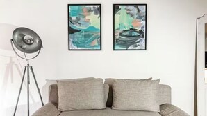 Un salón moderno con un sofá gris, dos cuadros abstractos y una lámpara de pie.