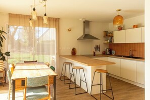 A modern kitchen with a central island, bar stools, and a dining area with a table and chairs. - House 4-8 pers. with large garden - Golfe du Morbihan - beaches & Vannes nearby (Le Hézo)