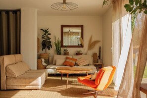 A living room with a sofa, a chair, a coffee table, and a large window with curtains. - House 4-8 pers. with large garden - Golfe du Morbihan - beaches & Vannes nearby (Le Hézo)