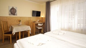 Une chambre d’hôtel avec deux lits, un bureau, une chaise, une télévision et un tableau au mur.