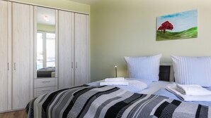 Een slaapkamer met een bed, gestreept beddengoed, een schilderij van een boom en een kledingkast.