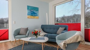 Een moderne woonkamer met een blauwe bank, twee fauteuils, een salontafel en een schilderij van een strandgezicht.