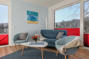 A modern living room with a blue sofa, two armchairs, a coffee table, and a painting of a beach scene. - Great view of the Nordperd - Villa Bergfrieden Terrassenhaus FeWo 04 - Villa (Göhren)