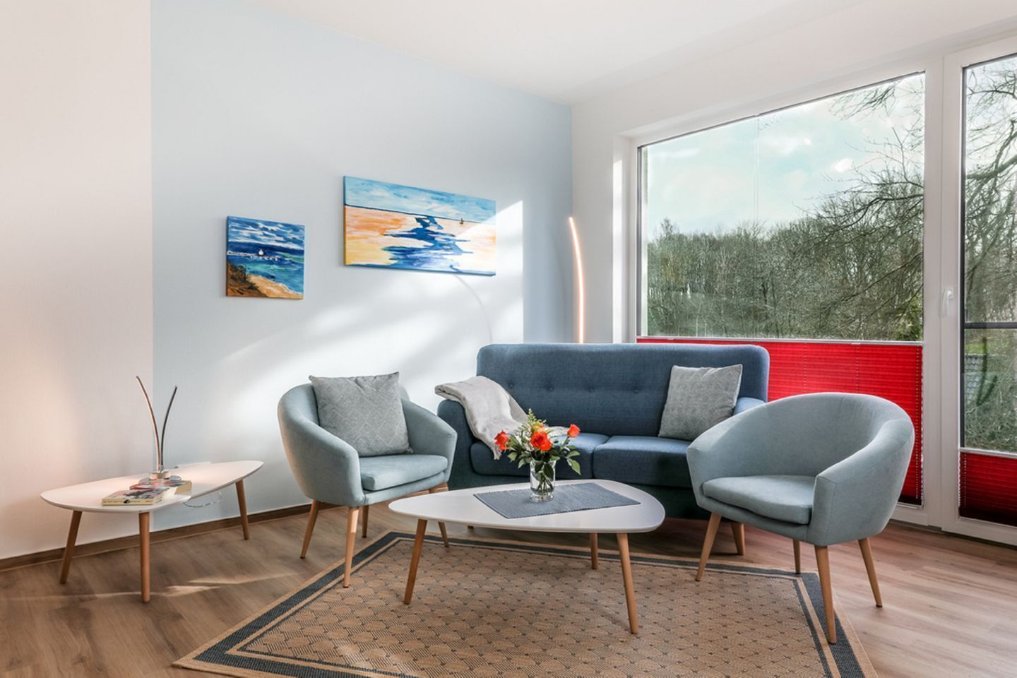 A modern living room with a blue sofa, two armchairs, a coffee table, and artwork on the wall.