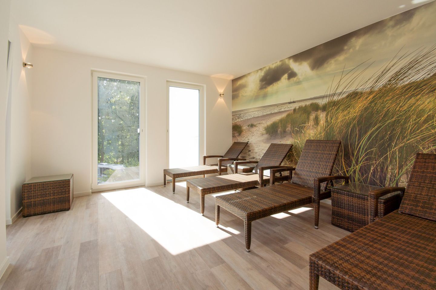 Une pièce baignée de lumière naturelle, meublée de mobilier en osier, dotée de grandes fenêtres et ornée d’une fresque représentant une plage.