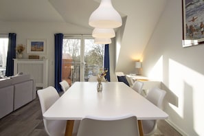 Un espace repas moderne avec une table blanche, des chaises blanches et un luminaire suspendu.