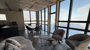 Ein modernes Interieur mit einem großen Esstisch, bequemen Sitzgelegenheiten und Meerblick durch große Fenster.