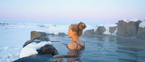 Una persona en un balneario con vistas a un paisaje nevado y grandes rocas.