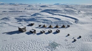 Eine verschneite Landschaft mit mehreren kleinen, kegelförmigen Bauwerken und einigen größeren Gebäuden.