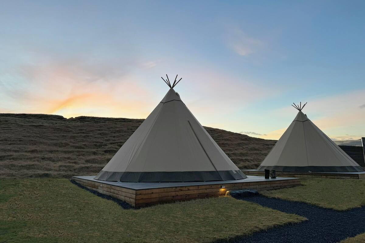 Dos tiendas tipo tipi con una plataforma de madera plana en un campo cubierto de hierba.