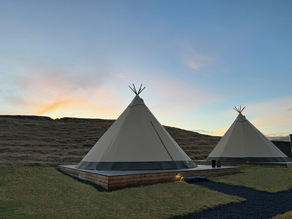 Two tipi-style tents with a flat wooden platform in a grassy field. - Sorla Camp (Rangarthing ytra)