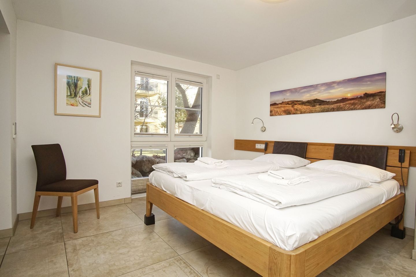 Ein Schlafzimmer mit einem Holzbett, weißer Bettwäsche, einem Sessel und einem Bild an der Wand.
