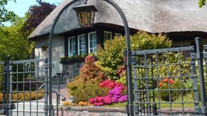 A thatched-roof house with a stone facade, a gated entrance, and a well-maintained garden with colorful flowers. - Rügen vacation near the beach - Landhaus Wilkens Bungalow Nordlicht - Country house (Baabe)