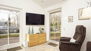 A modern living room with a flat-screen TV, a brown leather chair, a wooden cabinet, and a glass coffee table. - Rügen vacation near the beach - Landhaus Wilkens Bungalow Nordlicht - Country house (Baabe)