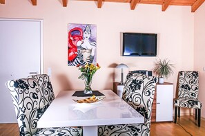 A dining area with a white table, patterned chairs, a painting, a TV, and a potted plant. - Quiet location and great view of the Nordperd - Villa Bergfrieden Süd FeWo 05 - (Göhren)