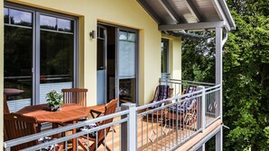 Ein Balkon mit Holztisch und -stühlen, einem Blumentopf und einem Geländer.