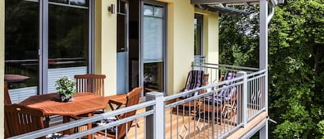 A balcony with a wooden table and chairs, a potted plant, and a railing.