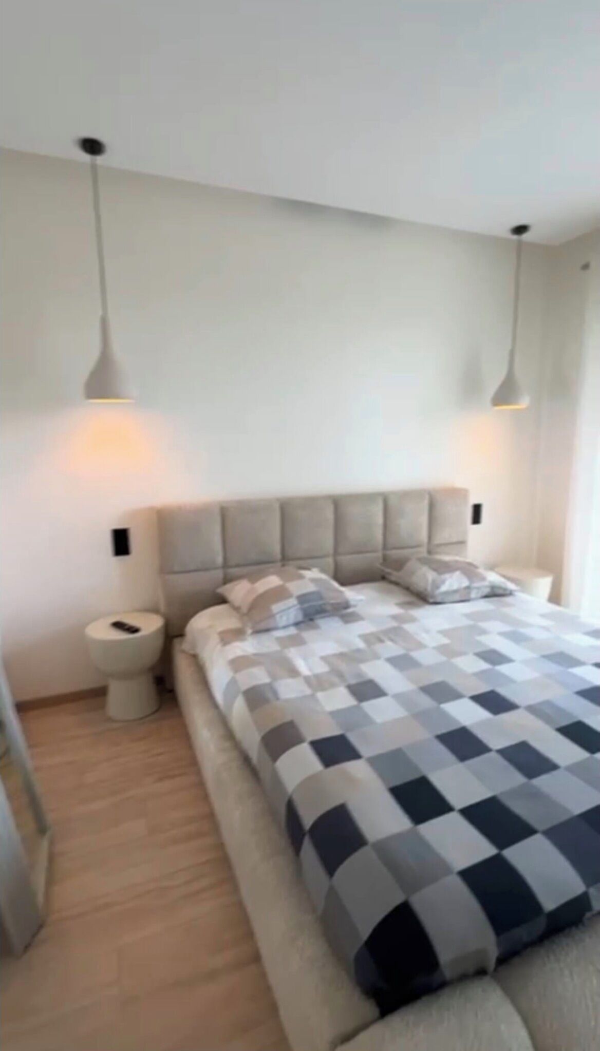 A modern bedroom with a large bed, two bedside tables, a nightstand, and a wall-mounted light fixture.