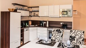 A compact kitchen with white cabinets, a microwave, a coffee maker, and a dining area with a table set for two. - Quiet location and great view of the Nordperd - Villa Bergfrieden Süd FeWo 03 - (Göhren)