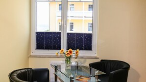 A dining area with a glass table and black chairs, a vase with flowers, and a window with blinds. - Quiet location and great view of the Nordperd - Villa Bergfrieden Süd FeWo 03 - (Göhren)