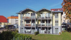 A multi-story residential building with balconies, a covered outdoor seating area, and a well-maintained lawn. - Quiet location and great view of the Nordperd - Villa Bergfrieden Süd FeWo 03 - (Göhren)