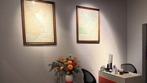 En receptionsdisk med en vase blomster, to indrammede kort på væggen og en computerskærm.