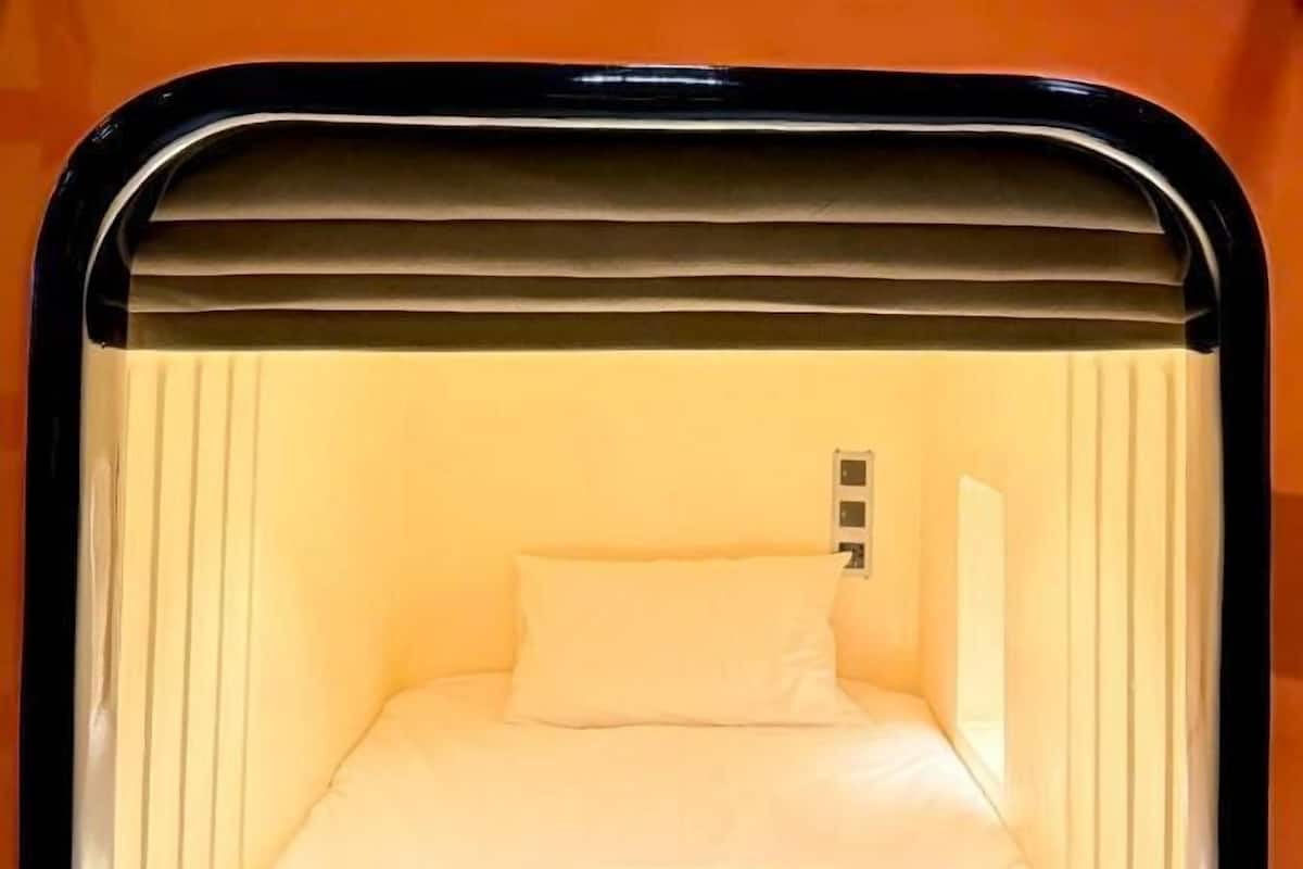 A small, enclosed room with a bed, a pillow, and a wall-mounted control panel.