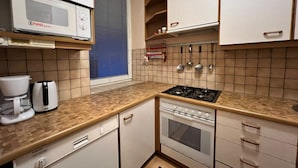 A compact kitchen with a microwave, coffee maker, stove, oven, and a window with blinds.