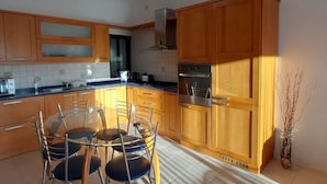 A kitchen with wooden cabinets, a stainless steel oven, and a glass dining table with chairs.