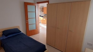 A bedroom with a bed, a wardrobe, and a door leading to a kitchen.