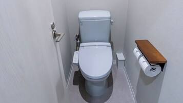 Un baño pequeño y estrecho con inodoro blanco, dispensador de papel higiénico y una estantería pequeña.