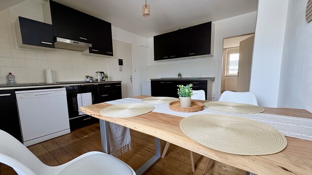 A modern kitchen with a wooden table, white chairs, and a small potted plant. - Modern Accommodation with Comfort & Prime Location (Holzwickede)