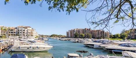 A marina with numerous boats docked along a waterfront, surrounded by buildings and greenery.