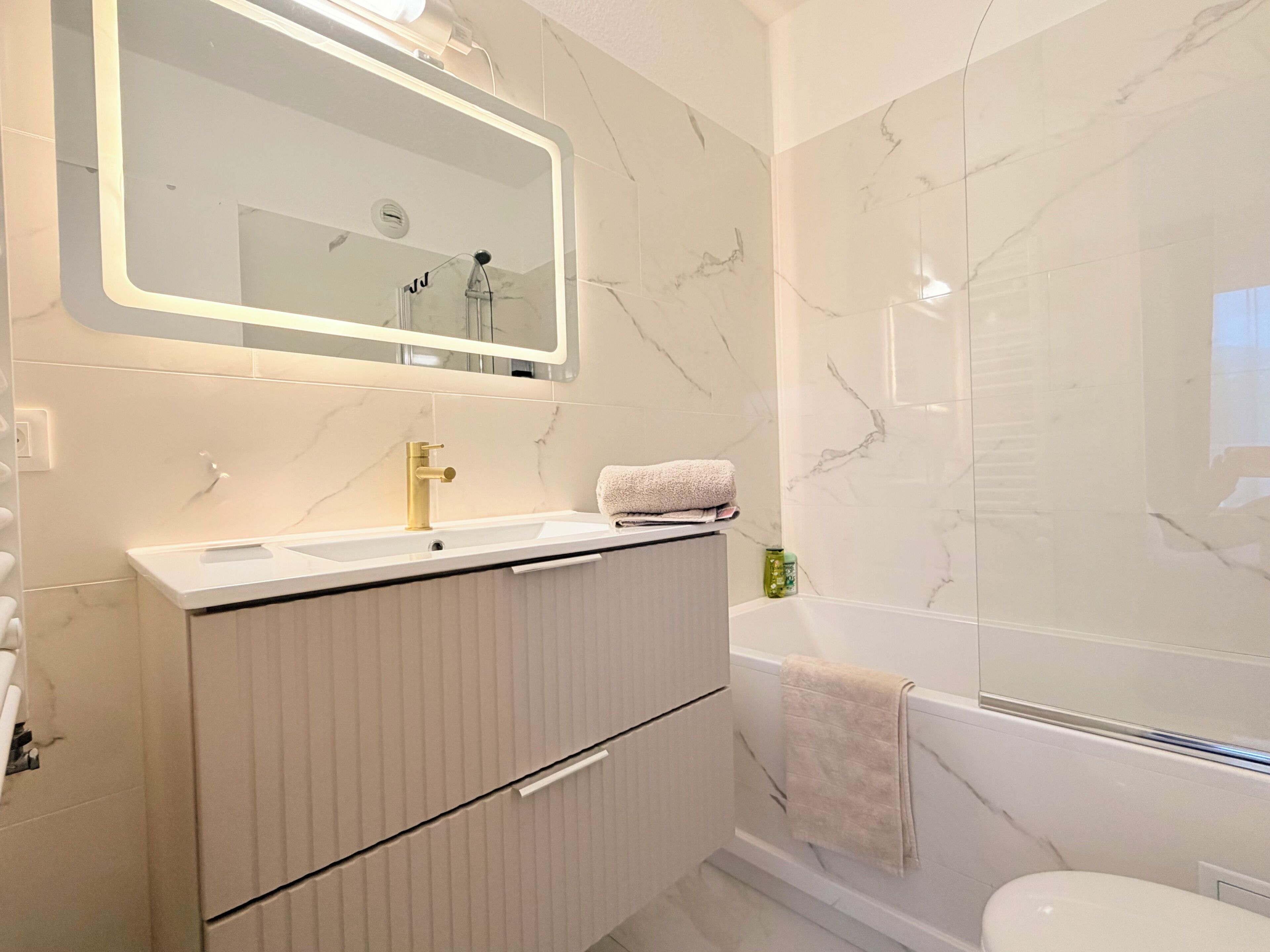 Un baño moderno con lavabo de mármol, grifo dorado, espejo y bañera.