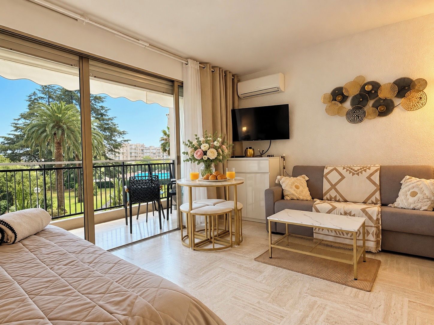 Een hotelkamer met een bed, een bank, een tafeltje, een televisie en een balkon met uitzicht op het zwembad.