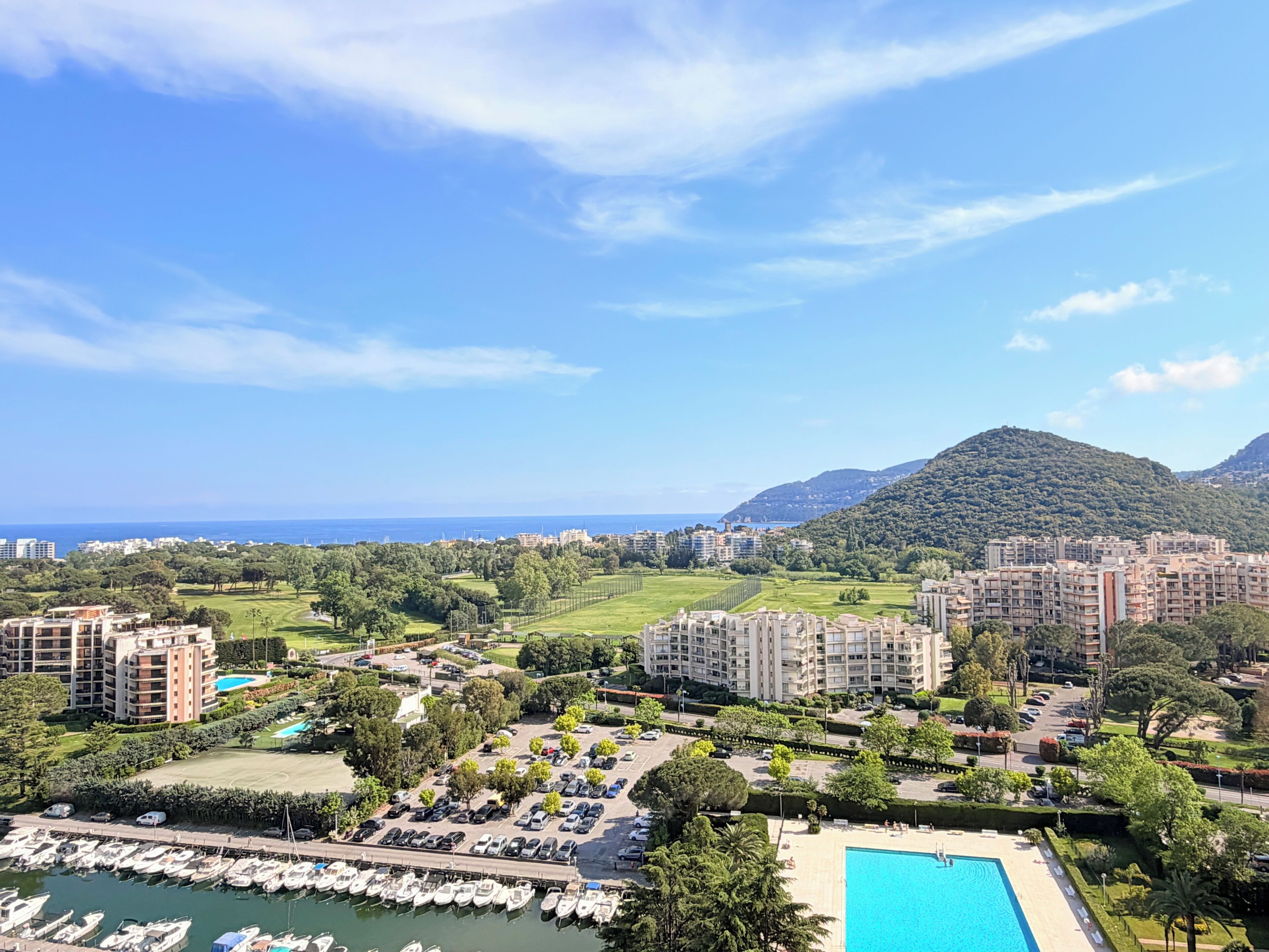 Un resort costero con un puerto deportivo, piscina y vistas al mar y a las montañas.
