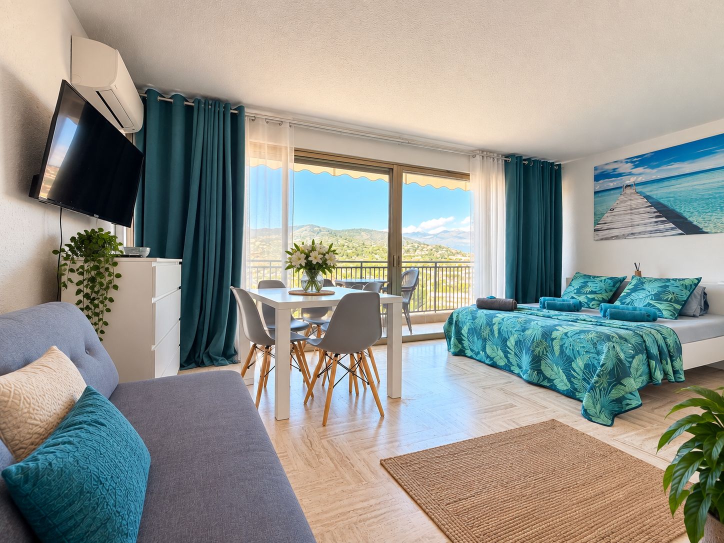 A modern room with a balcony, a dining area, and a bed with a tropical-themed bedspread.