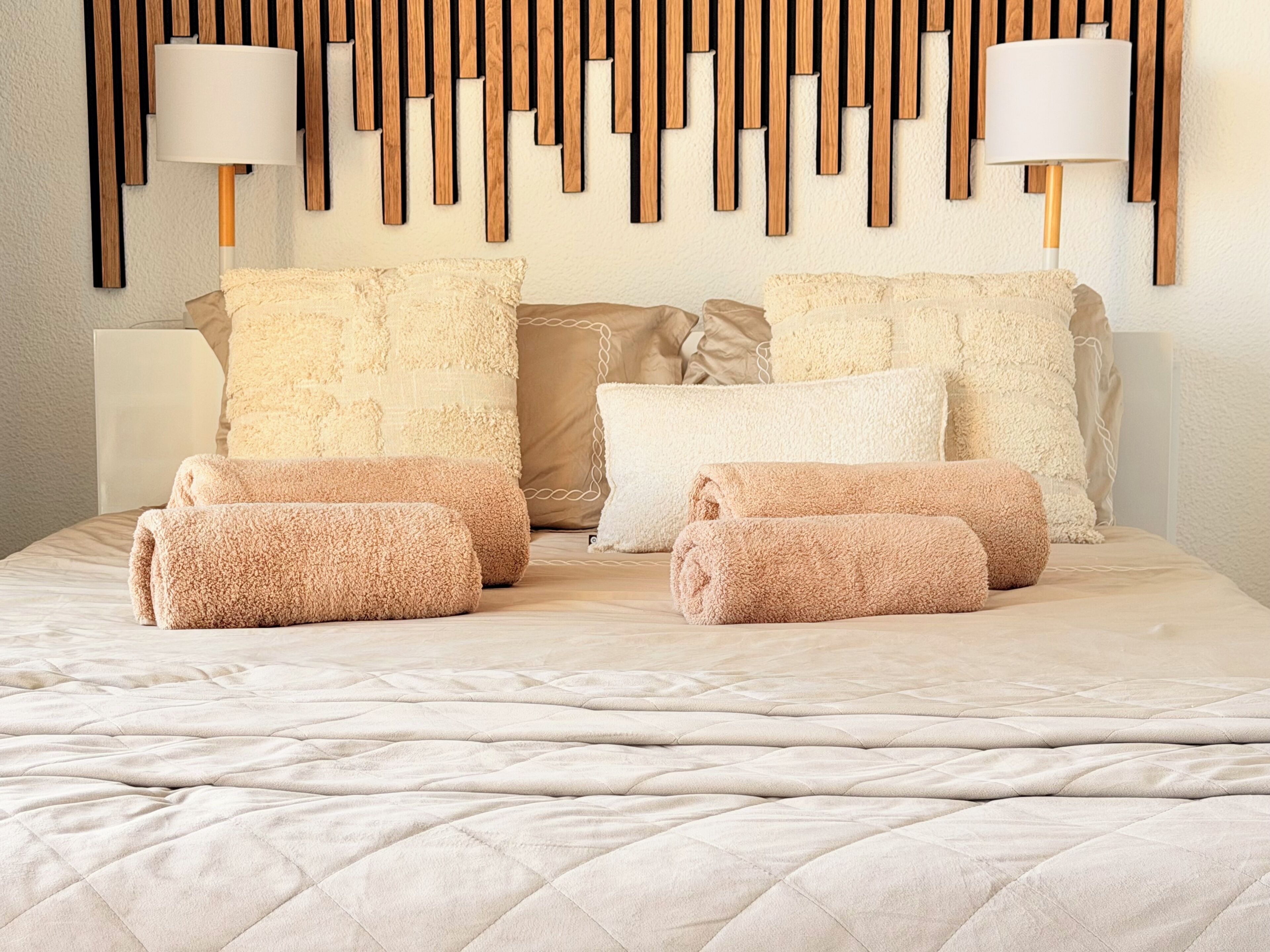 Ein Bett mit gesteppter Bettdecke, mehreren Kissen und aufgerollten Handtüchern.