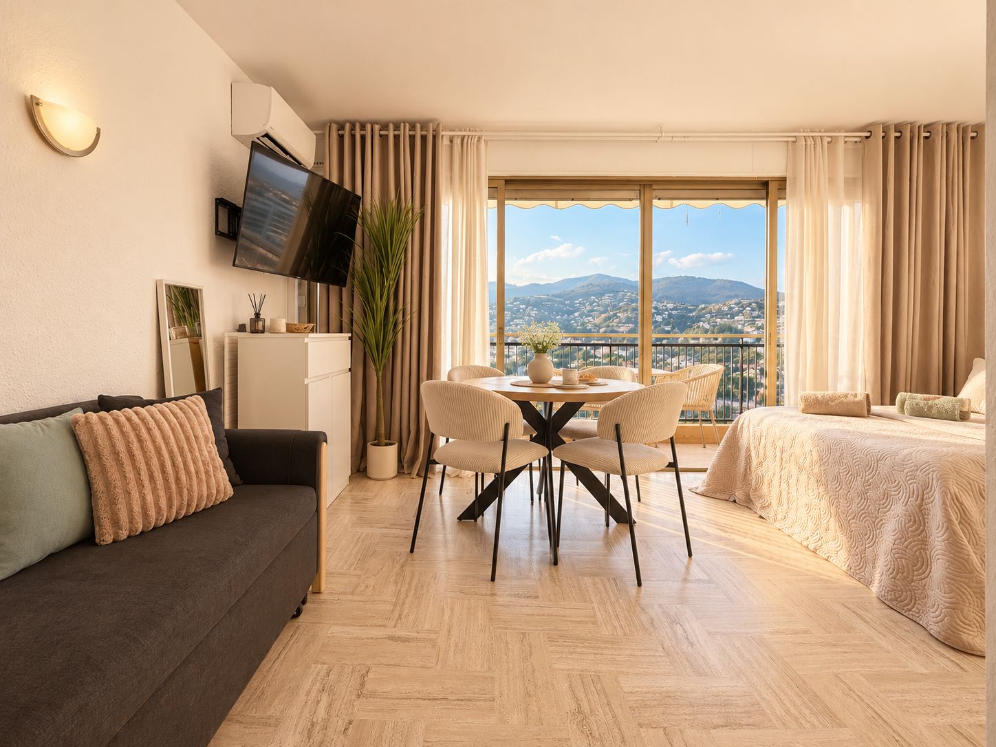 A modern hotel room with a dining area, a sofa, a bed, and a large window offering a city view.